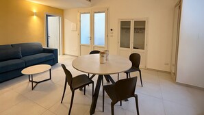 A modern living room with a sofa, a round dining table with chairs, and a staircase leading to an upper level. - Molo Mazzini (Gallipoli)