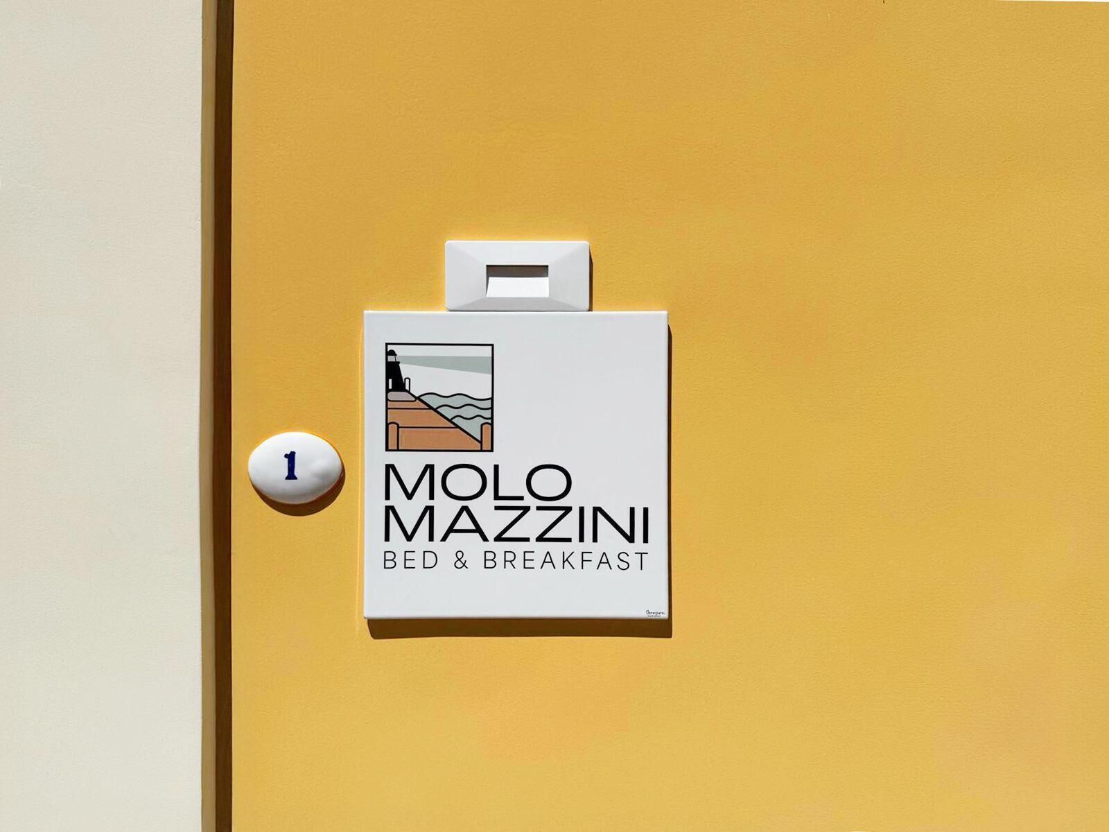 Une porte avec une enseigne indiquant « Molo Mazzini Bed & Breakfast » et un chiffre « 1 » sur un carillon blanc.