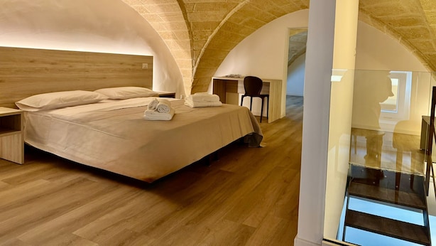 A bedroom with a wooden headboard, a bed with white linens, a bedside table, and a chair. - Molo Mazzini (Gallipoli)