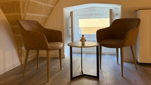 A loft bedroom with a sloped ceiling, two brown chairs, a small round table, and a window with a view. - Molo Mazzini (Gallipoli)