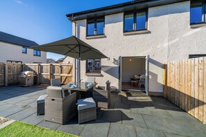 Eine Terrasse mit Gartenmöbeln, einem Grill und einem überdachten Bereich.