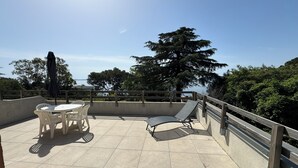 Una terraza con mesa y sillas, un sillón de sol y vistas al mar.
