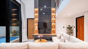 Un moderno salón con sofá, televisor y vistas a la piscina.