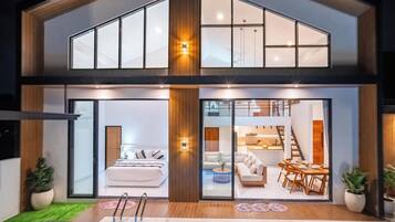 Une maison moderne à deux étages, avec une chambre, un salon et un espace repas visibles de l’extérieur.