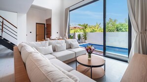 Una sala de estar moderna con un sofá modular grande, una mesa redonda y vista a una piscina.