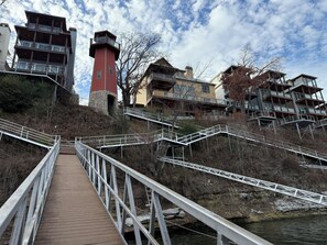 Un puente de madera que lleva a un edificio con una torre roja, rodeado de árboles y un río.