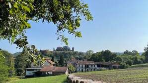 Paisagem rural com fardos de feno, uma casa de campo e um edifício no topo da colina.