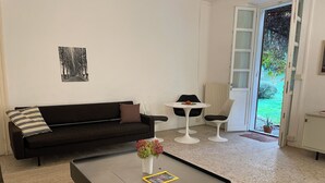 Uma sala de estar moderna com sofá, mesa de centro, uma pequena mesa redonda com cadeiras e uma porta que dá para o exterior.