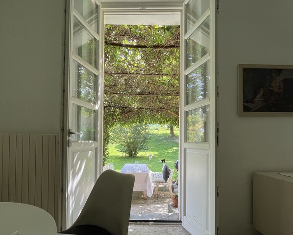 An open door leading to a garden with a table and chairs, a person in the distance, and a painting on the wall.