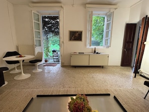 A room with a dining table, chairs, a small cabinet, and a view of the outdoors.