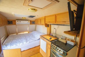Un intérieur de camping-car compact comprenant un lit, un coin cuisine et un petit réfrigérateur.