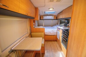 Ein kompaktes Wohnmobil-Interieur mit Küchenzeile, einem Bett und einer kleinen Essecke.