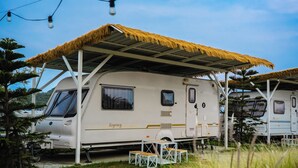 Una caravana con techo de paja, una mesa y sillas afuera.