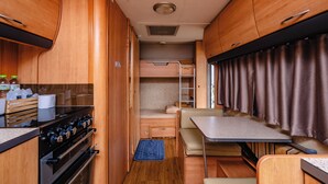 Interior compacto de una caravana con kitchenette, una cama y zona de comedor.