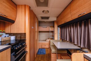 Un intérieur de camping-car compact comprenant un coin cuisine, un lit et un espace repas.