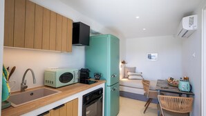 Eine kompakte Küche mit Spüle, Mikrowelle, Toaster und Backofen. Es gibt einen türkisblauen Kühlschrank, einen Esstisch mit Stühlen und eine kleine Sitzecke mit einer Couch.