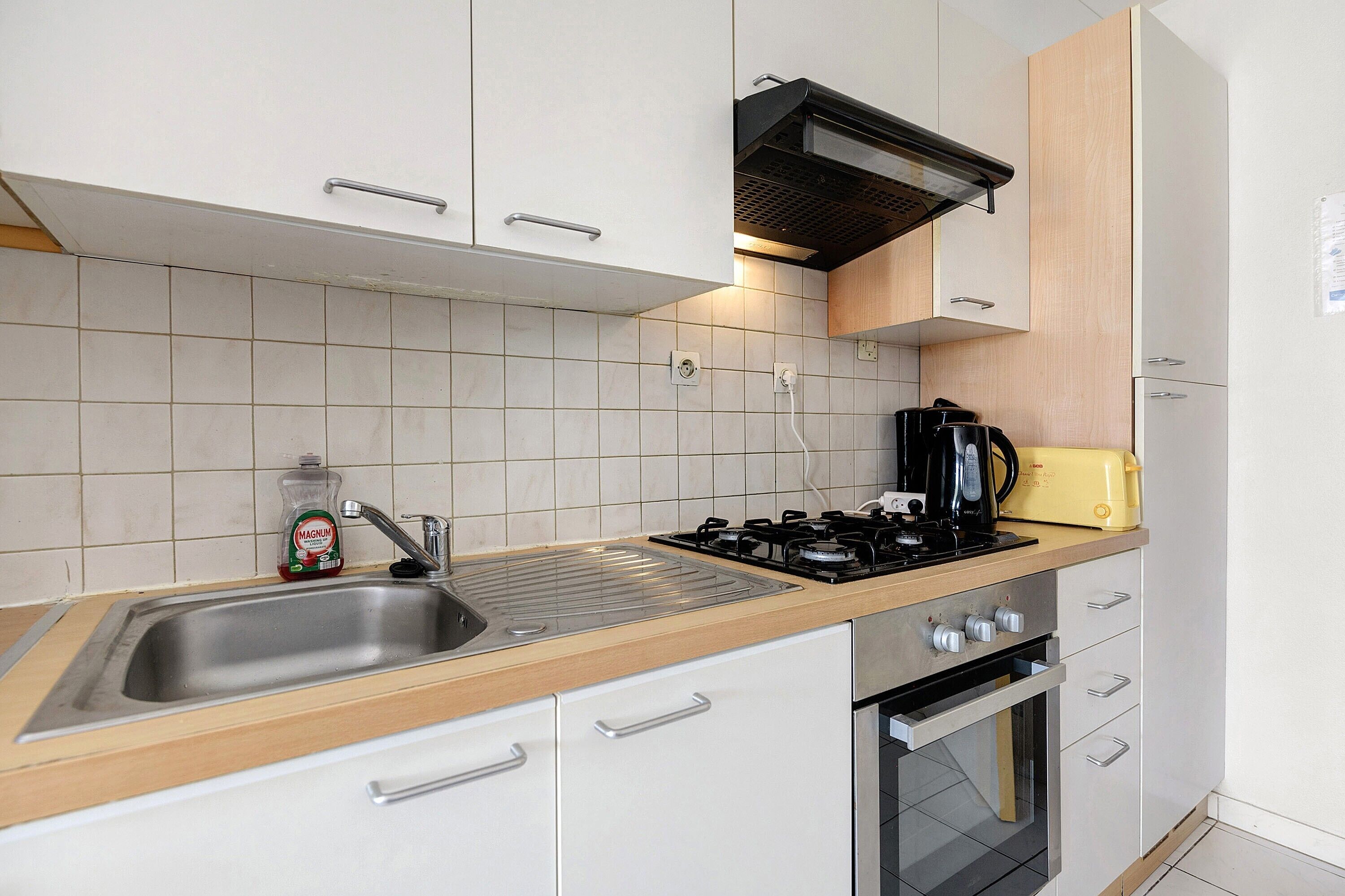 A modern kitchen with a stainless steel sink, a gas stove, a built-in oven, and wooden cabinets.