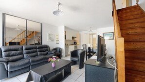 A modern living room with a sofa, coffee table, and chairs, a kitchen area, and a wooden staircase.