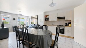 A modern kitchen with white cabinets, a dining table with chairs, and a visible clock on the wall.
