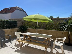Un patio con una mesa y sillas, una sombrilla verde y vistas al cielo.