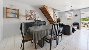 A dining area with a table, chairs, a wooden staircase, a kitchen area, and a view through a glass door.