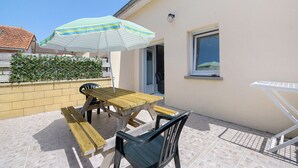 A patio with a wooden table and chairs, a striped umbrella, and a white folding chair.