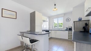 A modern kitchen with a bar area, white cabinetry, and a large window. - Gîte des Pluviers – Modern Villa Near the Beach in Saint-Martin-de-Bréhal (Bréhal)