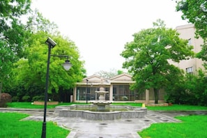 A courtyard with a fountain, a lamp post, and a building with a glass facade.