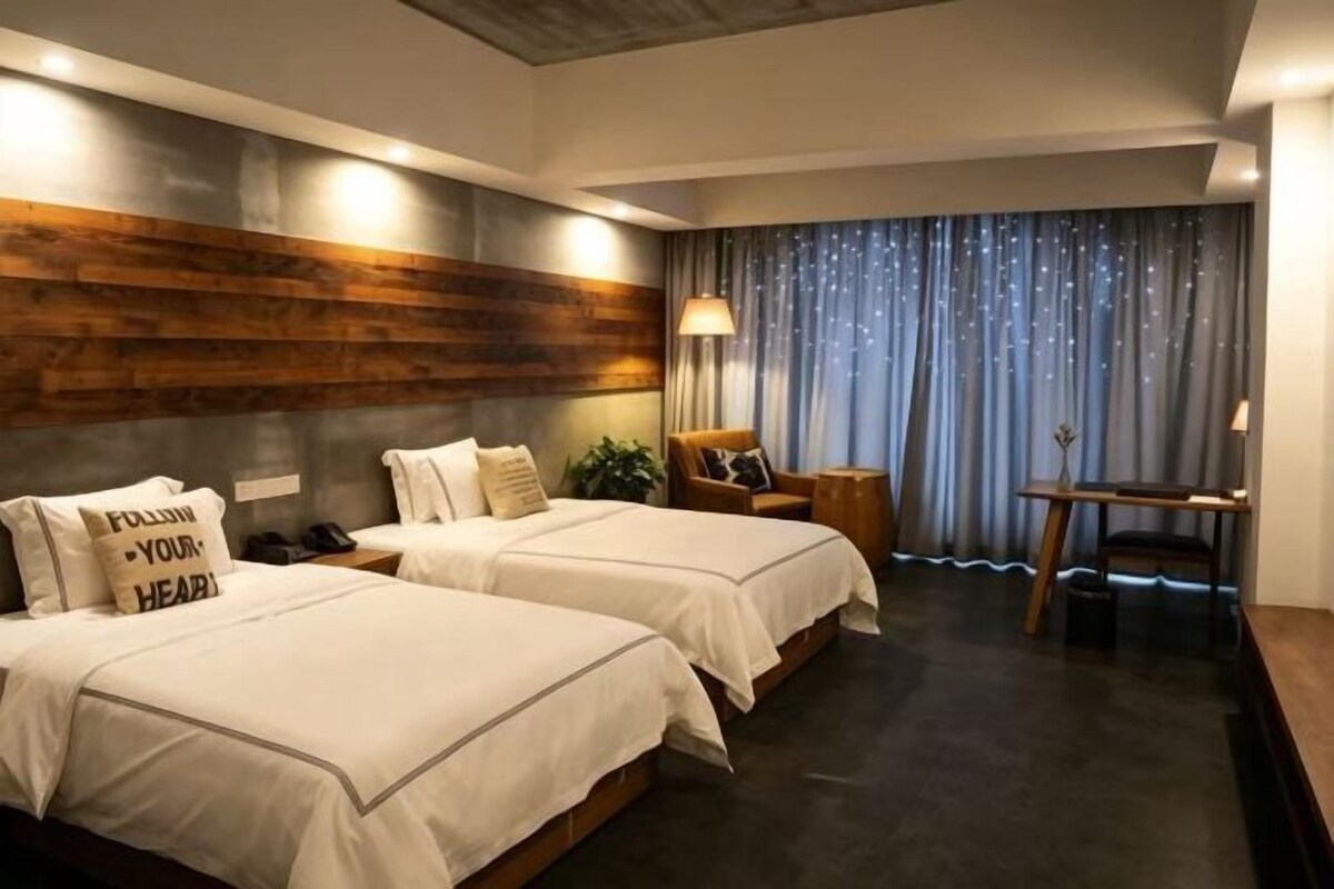A hotel room with two beds, a desk, a chair, a lamp, and a curtain.