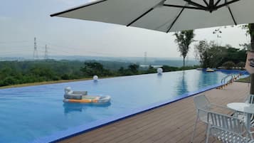 An infinity pool with a view of the landscape, a lounge area with a table and chairs, and a large umbrella providing shade.
