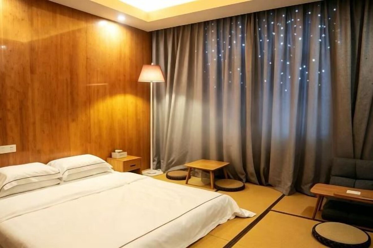 A hotel room with a bed, bedside table, lamp, and a view of the night sky through curtains.