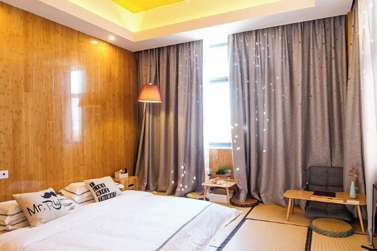 Habitación de hotel con una cama grande, un escritorio, una silla y un ventanal con cortinas.