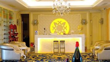 A hotel lobby with a reception desk, seating area, and a chandelier.