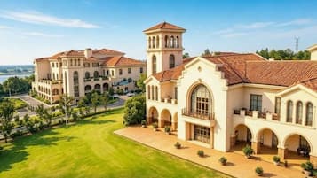 A large, historic building with multiple wings and a central tower, surrounded by well-maintained lawns and a clear sky.