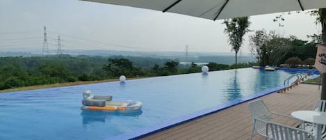 An infinity pool with a view of the landscape, a lounge area with chairs, and a large umbrella.