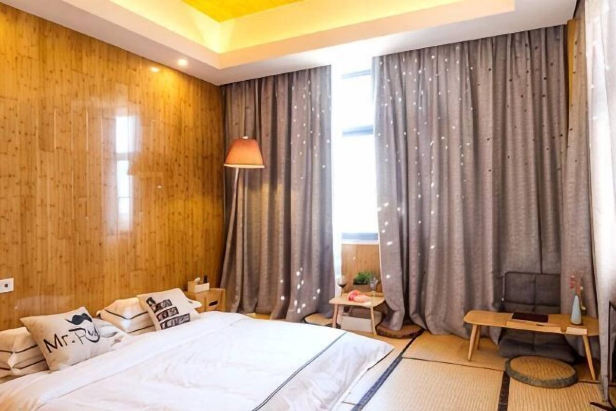Una habitación de hotel con una cama, cortinas, una lámpara, una mesita y un sofá.