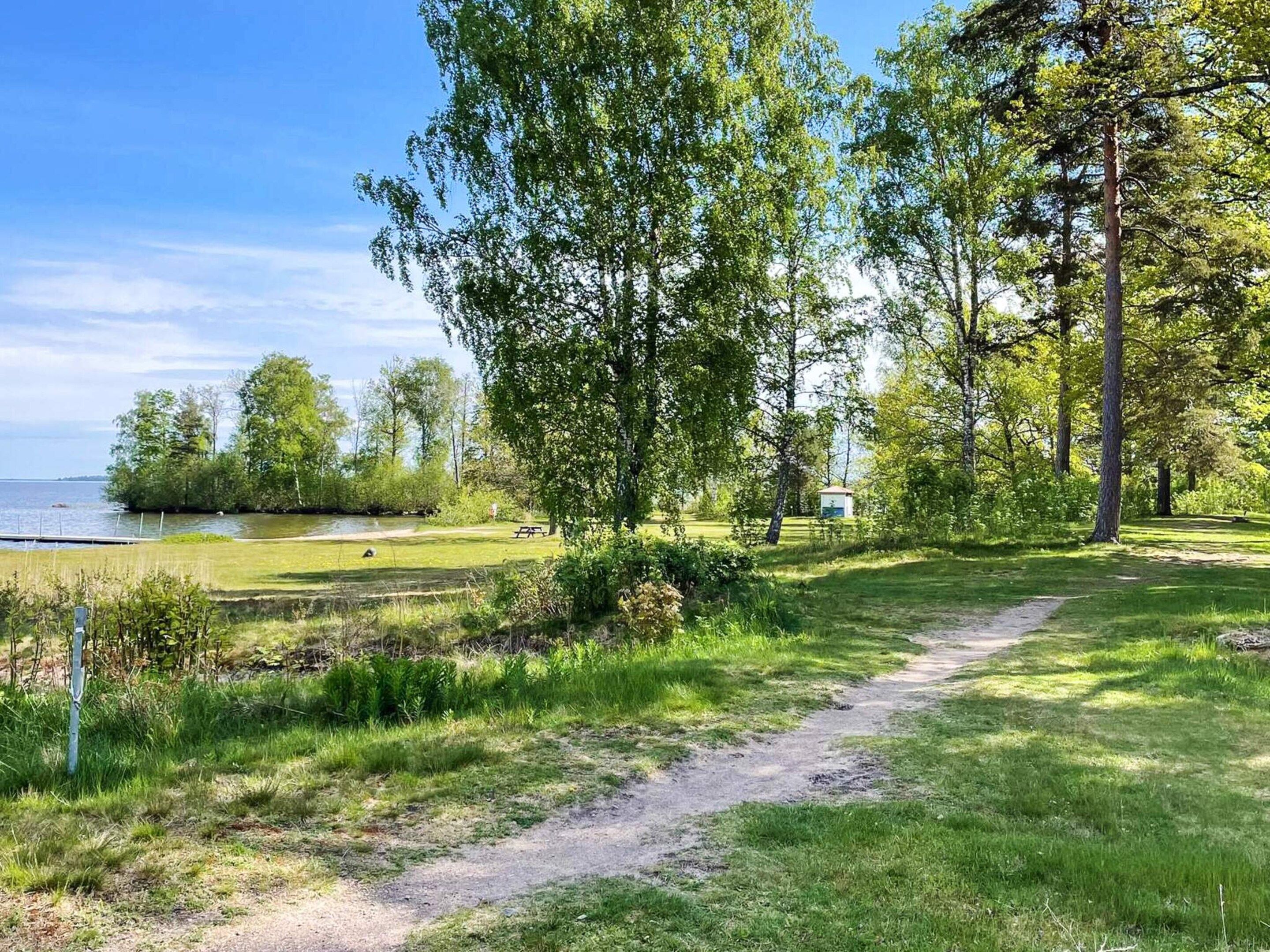 A pathway leading to a body of water with trees and a picnic area.