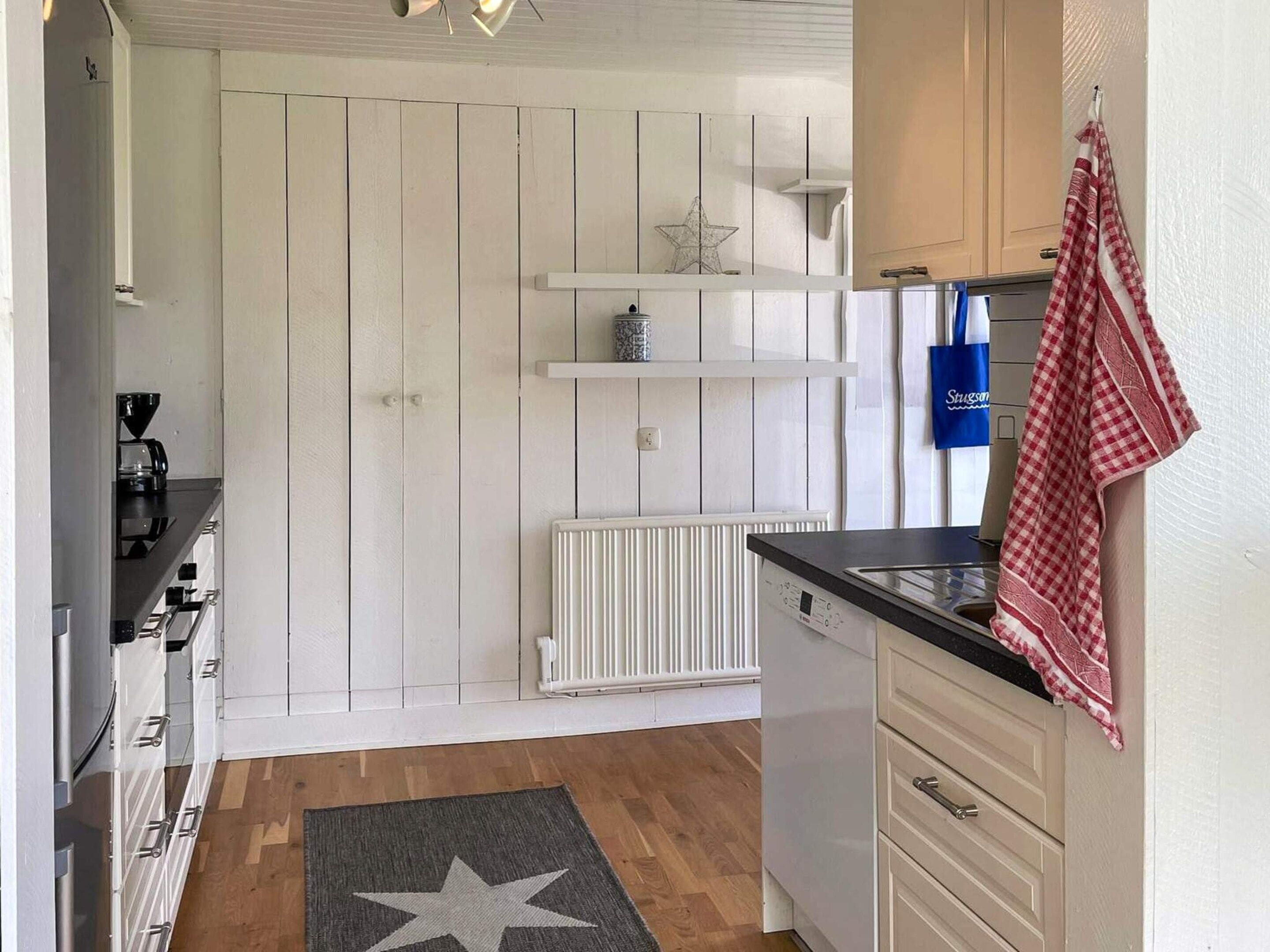 Una cocina con armarios blancos, encimera negra, alfombra con estampado de estrellas y un bolso azul colgado en la pared.