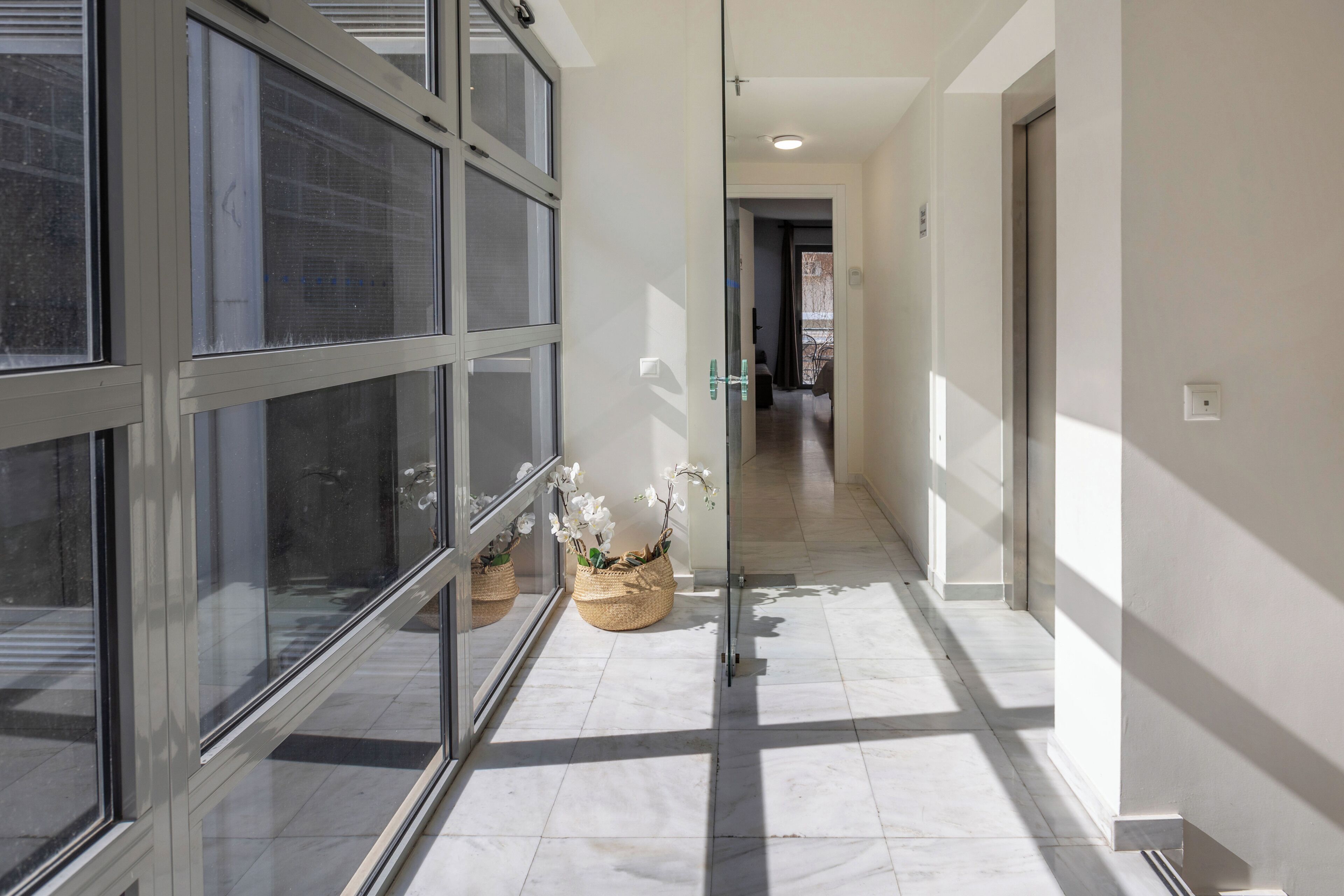 A hallway with glass doors, a tiled floor, and wicker baskets with flowers.