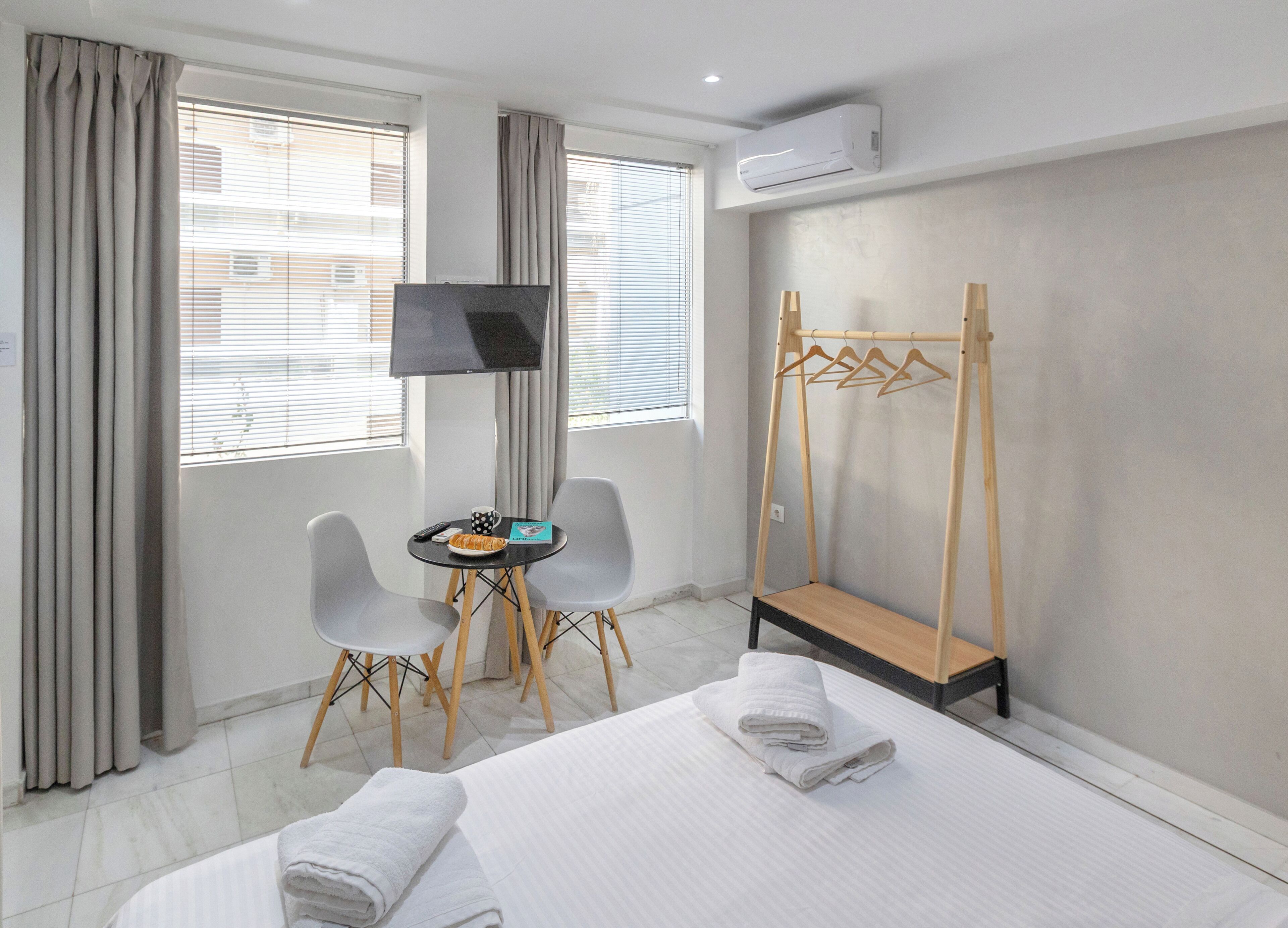 Habitación de hotel con cama, televisión, una mesita con control remoto, una silla y perchero de madera.