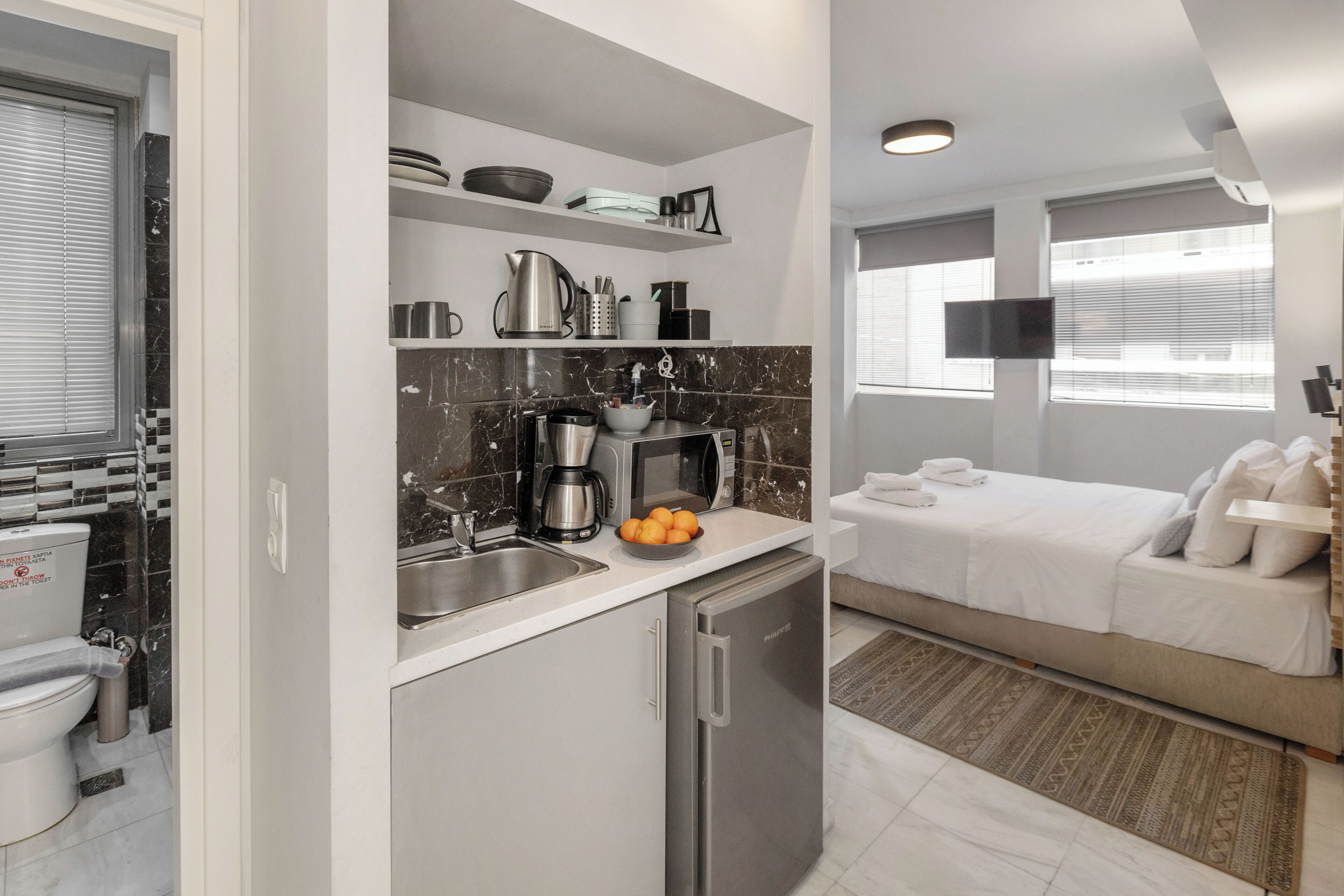 A compact hotel room with a kitchenette, a bed, a TV, and a bathroom.