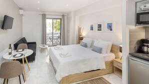 Een moderne hotelkamer met een bed, een eethoek, een televisie en een kitchenette.