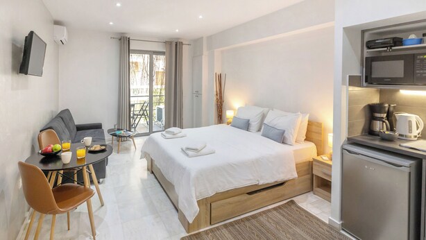 Hotelkamer met een bed, bureau met stoel, eettafel en een keukenhoek met een magnetron en kleine koelkast.