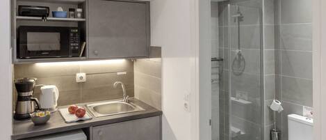 A modern kitchen with a microwave, coffee maker, and sink, and a separate shower area with a glass door.