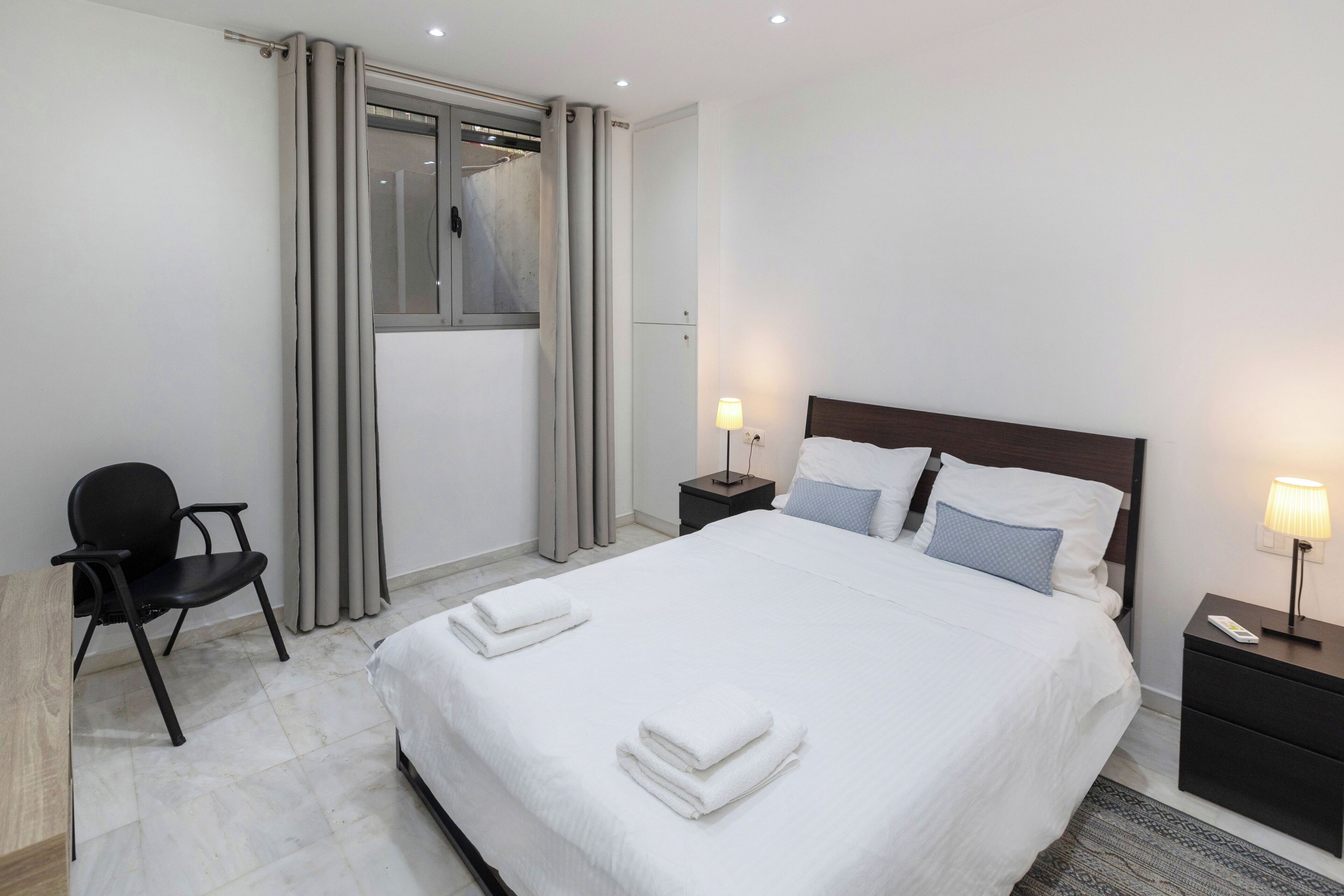 A hotel room with a bed, two bedside tables, a chair, a desk, and a window with curtains.