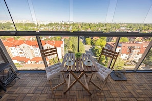 Ein Balkon mit einem Holztisch, zwei Stühlen und Blick auf eine Stadtlandschaft.