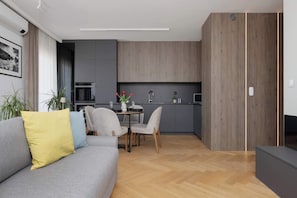 Ein modernes Wohnzimmer mit grauem Sofa, einem Esstisch mit Stühlen, einer Küchenzeile mit grauen Schränken und Holzboden.
