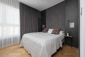 Ein Schlafzimmer mit Bett, Nachttisch, Fenster mit Vorhängen und einem Bild an der Wand.
