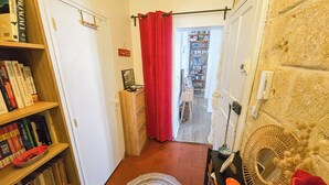 A narrow hallway with a wooden bookshelf, a red curtain, a small easel with artwork, and a stone wall with a mirror and decorative items. - C'est toi, chez moi - Apartment in the heart of Sète (Sète)