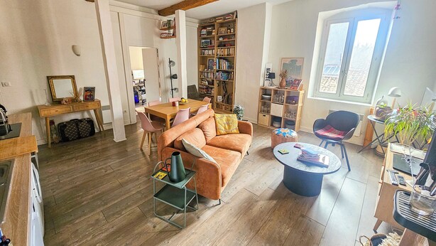 A spacious living area with a wooden floor, a sofa, a coffee table, a bookshelf, and a dining table. - C'est toi, chez moi - Apartment in the heart of Sète (Sète)